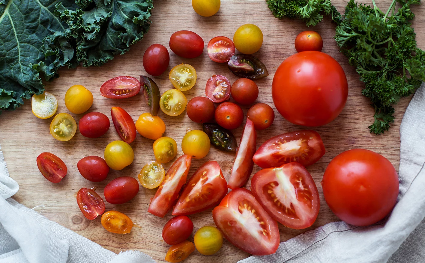 Kuvassa on puulaudalla erilaisia tomaatteja.