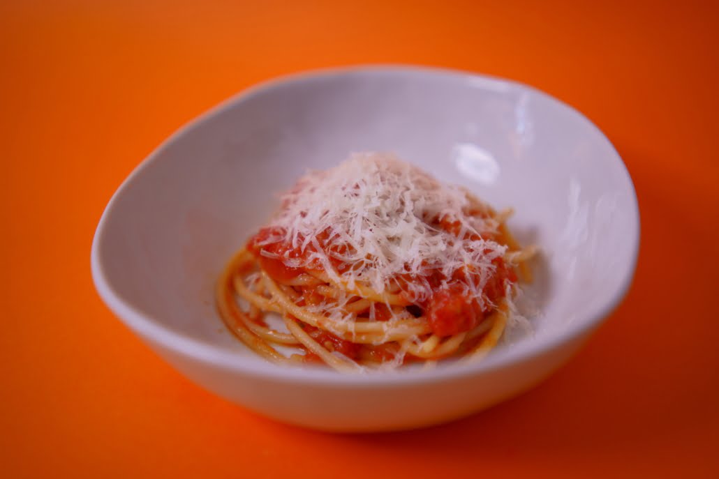 Kuvassa on valkoisessa keittolautasessa spagetti marinaraa. Kuvan tausta on oranssi.
