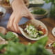 Kuvassa on käsi, joka nostaa täytettyä tacoa.