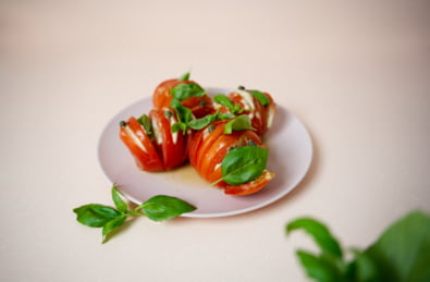 Kuvassa on valkoisella lautasella hasselbackan tomaatteja. Kuvan tausta on valkoinen.