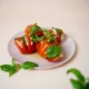 Kuvassa on valkoisella lautasella hasselbackan tomaatteja. Kuvan tausta on valkoinen.