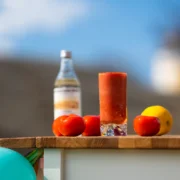 Kuvassa on pöydällä lasissa Bloody Marya, tomaatteja, sitruuna ja kirkas pullo.