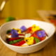 Kuvassa on valkoisella syvällä lautasella insalata capreseä, joka on koristeltu syötävillä orvokeilla.