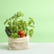 Kuvassa on kangaspussissa basilikaa, kurkkua, tomaattia ja salaattia. Kuvan tausta on vihreä.